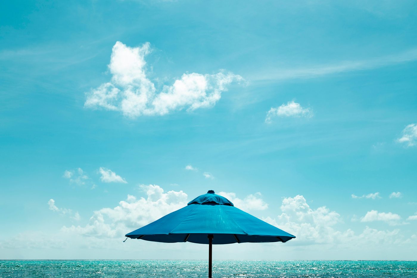Blue parasol on a serene Caribbean beach under a clear sky, perfect for summer vacations.
